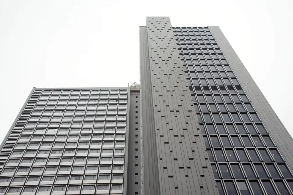 Perspective en gros plan d’une tour moderne de grande hauteur avec des façades géométriques épurées et des fenêtres répétitives.