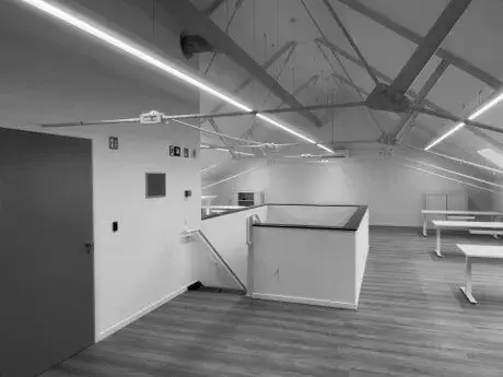 Gerenoveerde kantoorruimte onder een schuin dak, met zichtbare dakspanten, led‑lijnverlichting, houten vloerafwerking en open werkplekken, als onderdeel van een interieurrenovatieproject.