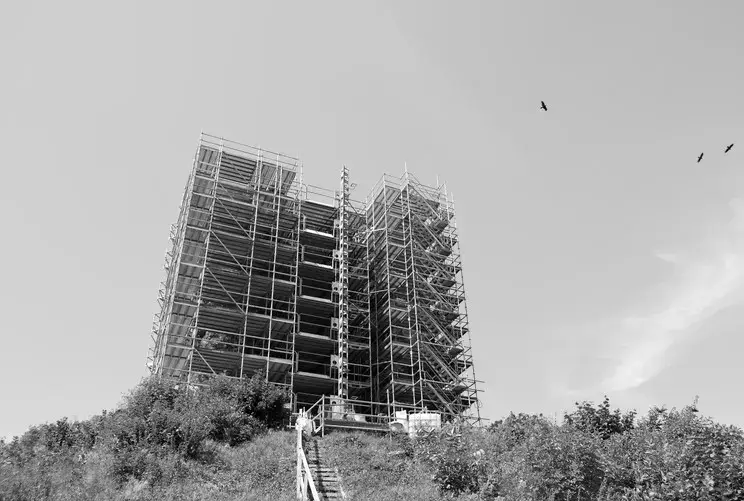 Groot steigercomplex rond een erfgoedsite op een heuvel, met tijdelijke trappen en omringende begroeiing, onderdeel van een gespecialiseerd restauratieproject.