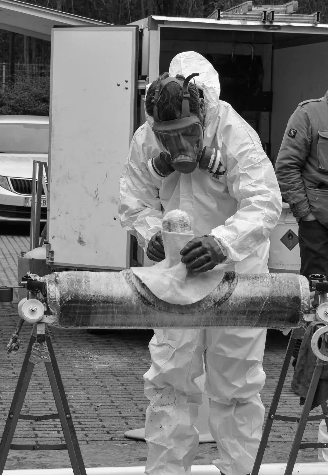 Medewerker in beschermende overall die een huisaansluitingsliner voorbereidt op een draagmal tijdens een rioolrenovatie‑ en kousreliningproces op een buitenterrein.