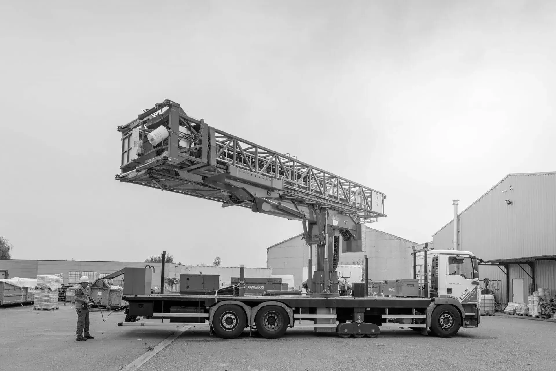 Laagtewerker met uitschuifbare inspectie‑ en onderbrugunit opgesteld op een industrieterrein, waarbij een medewerker naast het voertuig staat tijdens test‑ of demonstratiewerkzaamheden voor inspectie‑ en onderhoudstoepassingen aan bruggen en kunstwerken.