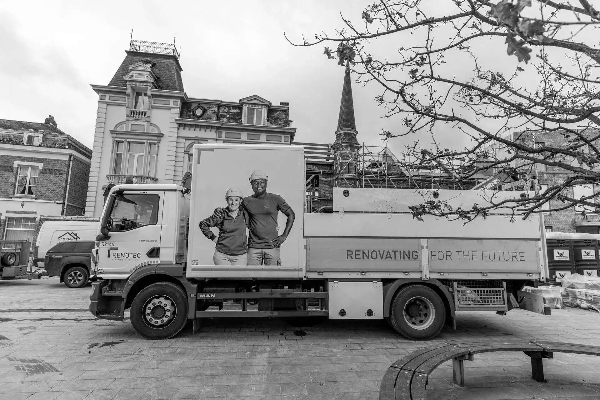 Renotec‑vrachtwagen met campagnevisual en de slogan ‘Renovating for the Future’ op een stadswerf, met historische gebouwen, steigers en werfactiviteiten op de achtergrond.