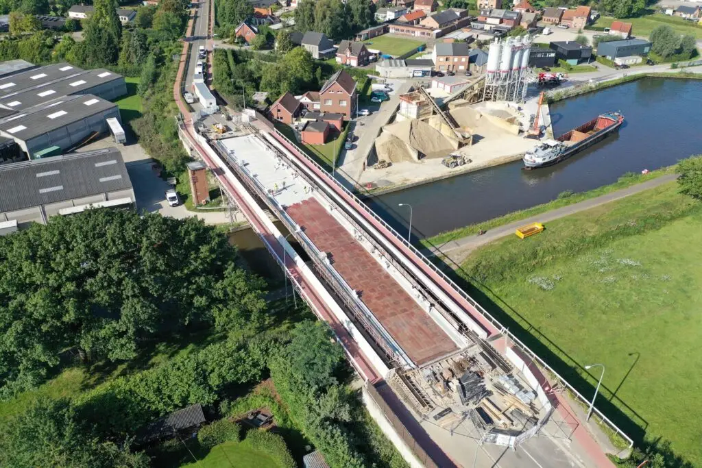 Luchtfoto van een brug in renovatie boven een waterweg, met zicht op betonwerken, werkzones en de omliggende infrastructuur. De afbeelding toont een werf waar Renotec instaat voor complexe infrastructuur- en brugrenovatiewerken.