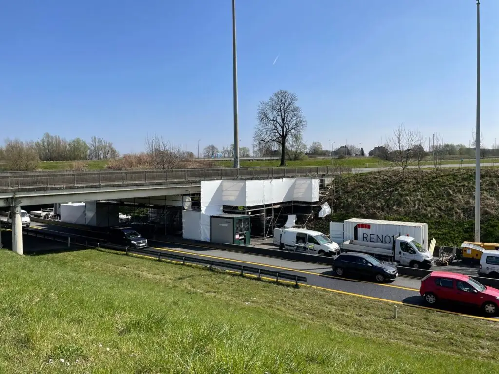 Hermetisch ingepakte stelling voor asbestsanering onder een brug, uitgevoerd door Renotec, met verkeer onder de werkzone.