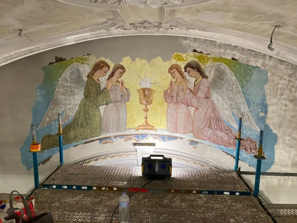 Restauratie van een historische religieuze muurschildering met engelen rond een kelk in een kapel, uitgevoerd door Renotec, zichtbaar op steigers tijdens gespecialiseerde erfgoed- en monumentenzorgwerken.