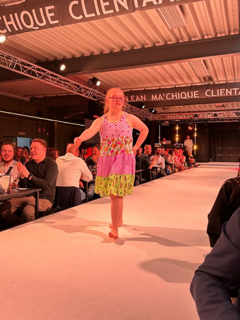Deelnemer loopt over catwalk tijdens benefietmodeshow in kader van Dag van de Liefdadigheid, met publiek en eventsetting – maatschappelijk engagement door Renotec