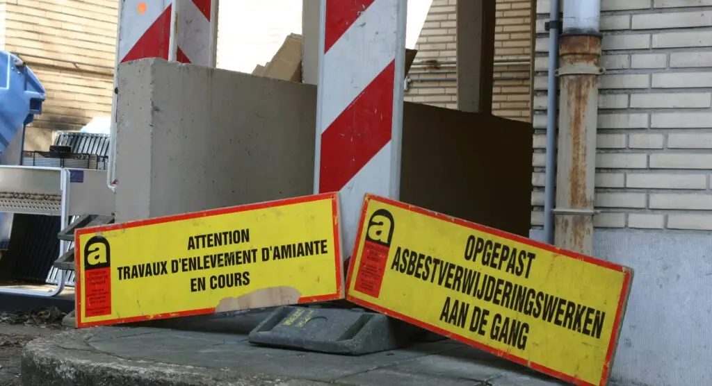 Signalisatie voor asbestwerken met waarschuwingsborden aan een afgesloten werfzone.