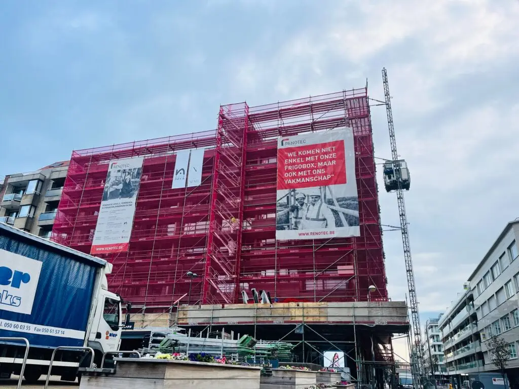 Renotec-werf met ingepakt gebouw in rode steigerdoeken, banner en kraan; renovatie van gevel en terrassen in Knokke