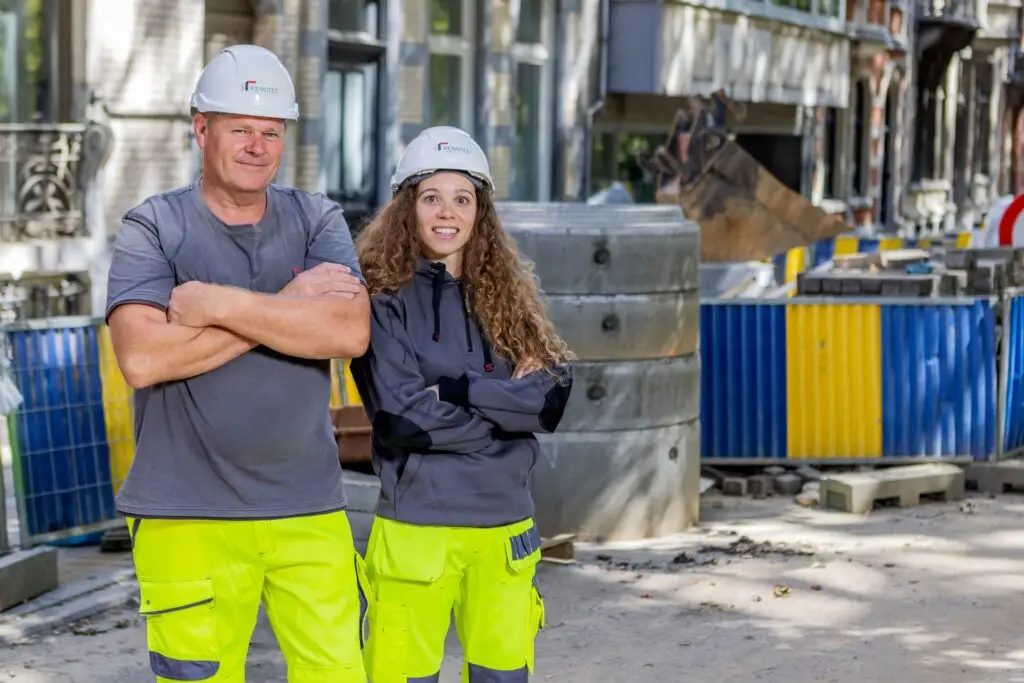 Renotec medewerkers op werf in stedelijke omgeving tijdens infrastructuur- en rioleringswerken met betonconstructie en werfmateriaal op de achtergrond