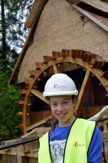 Leerling met Renotec-helm en fluohesje bij houten watermolen tijdens restauratieproject